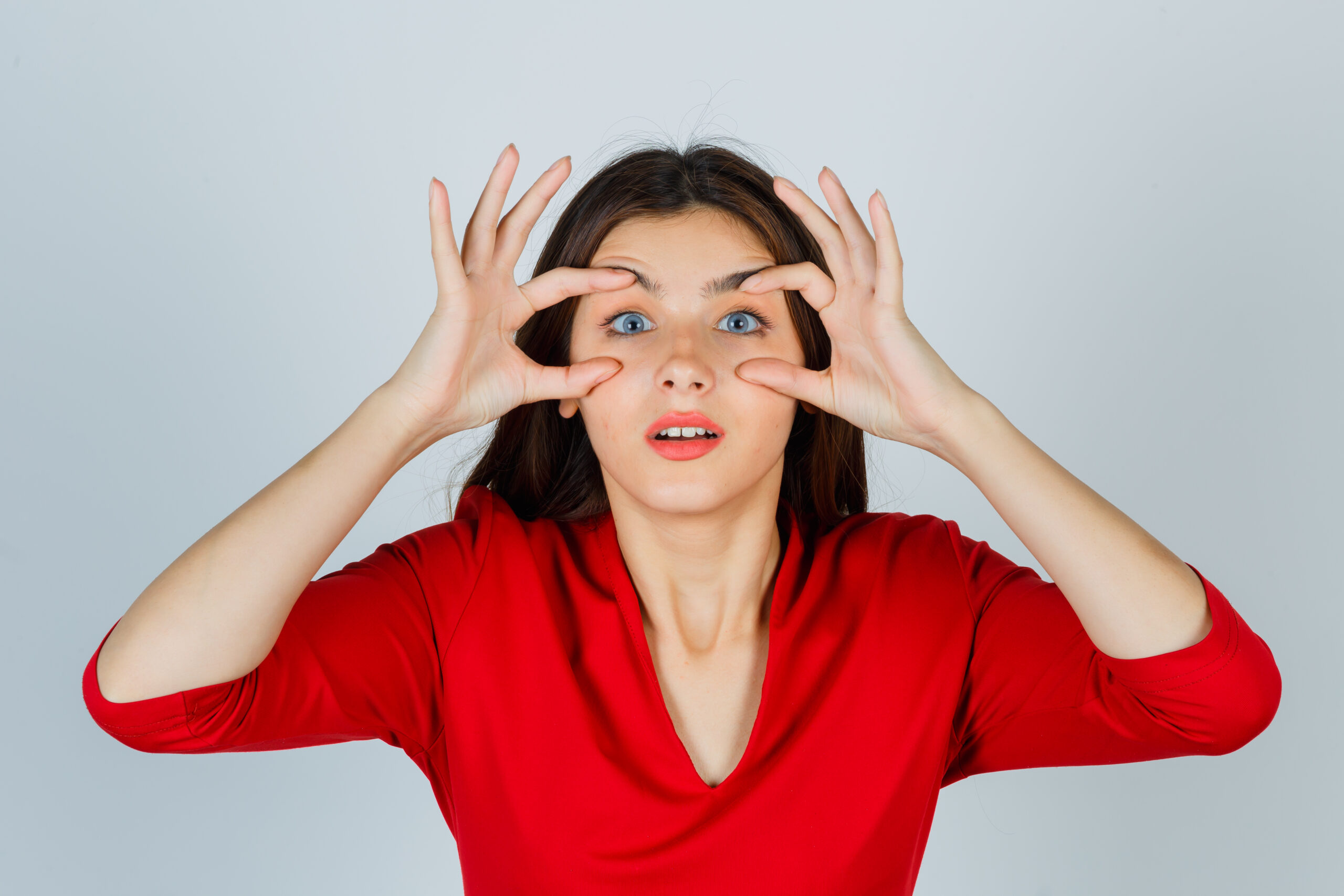 young lady opening eyes to see clearly in red blouse and looking pretty. front view.